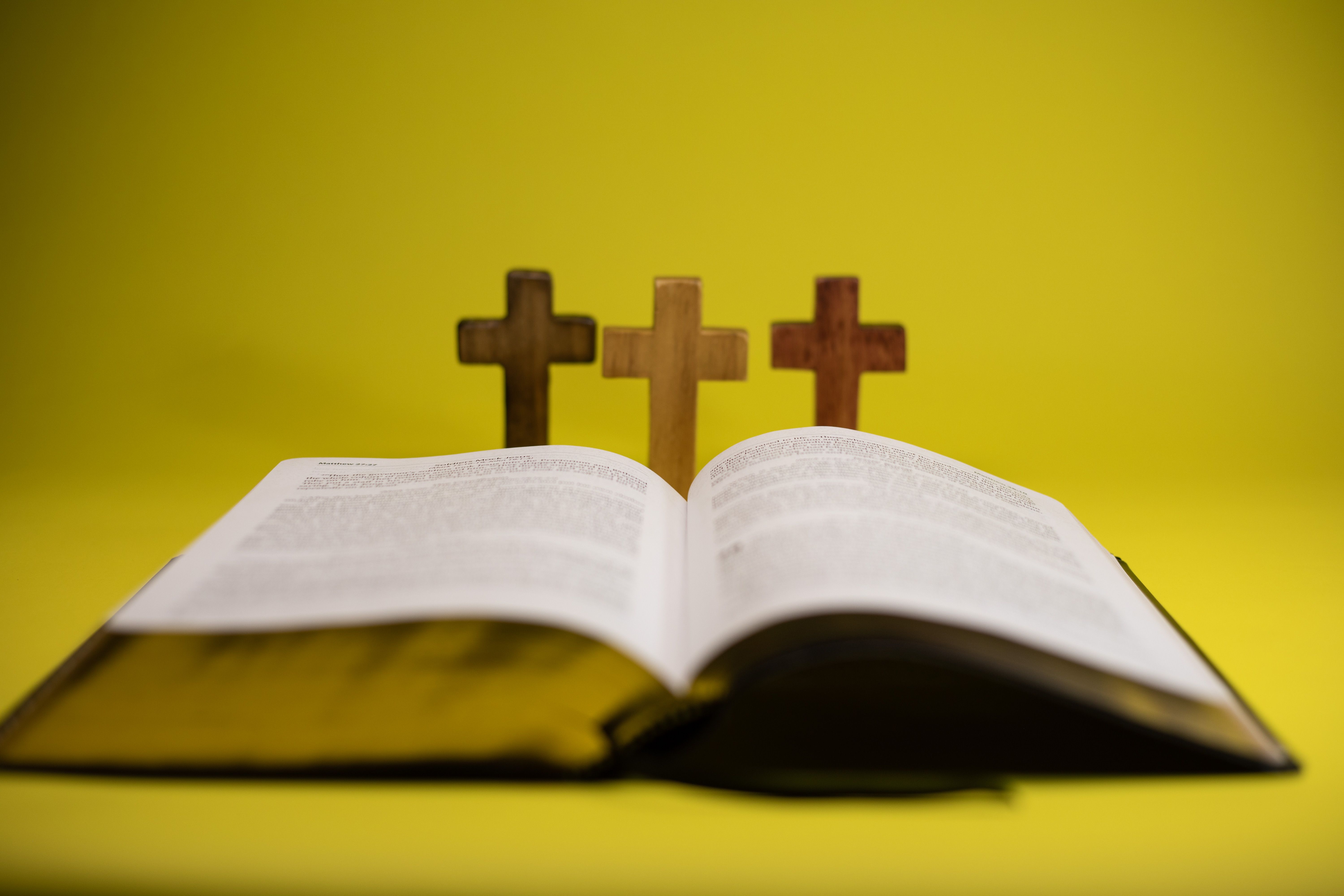 An open Bible with three crosses displayed against a vibrant yellow backdrop. — Foto: Philip Wels / Pexels