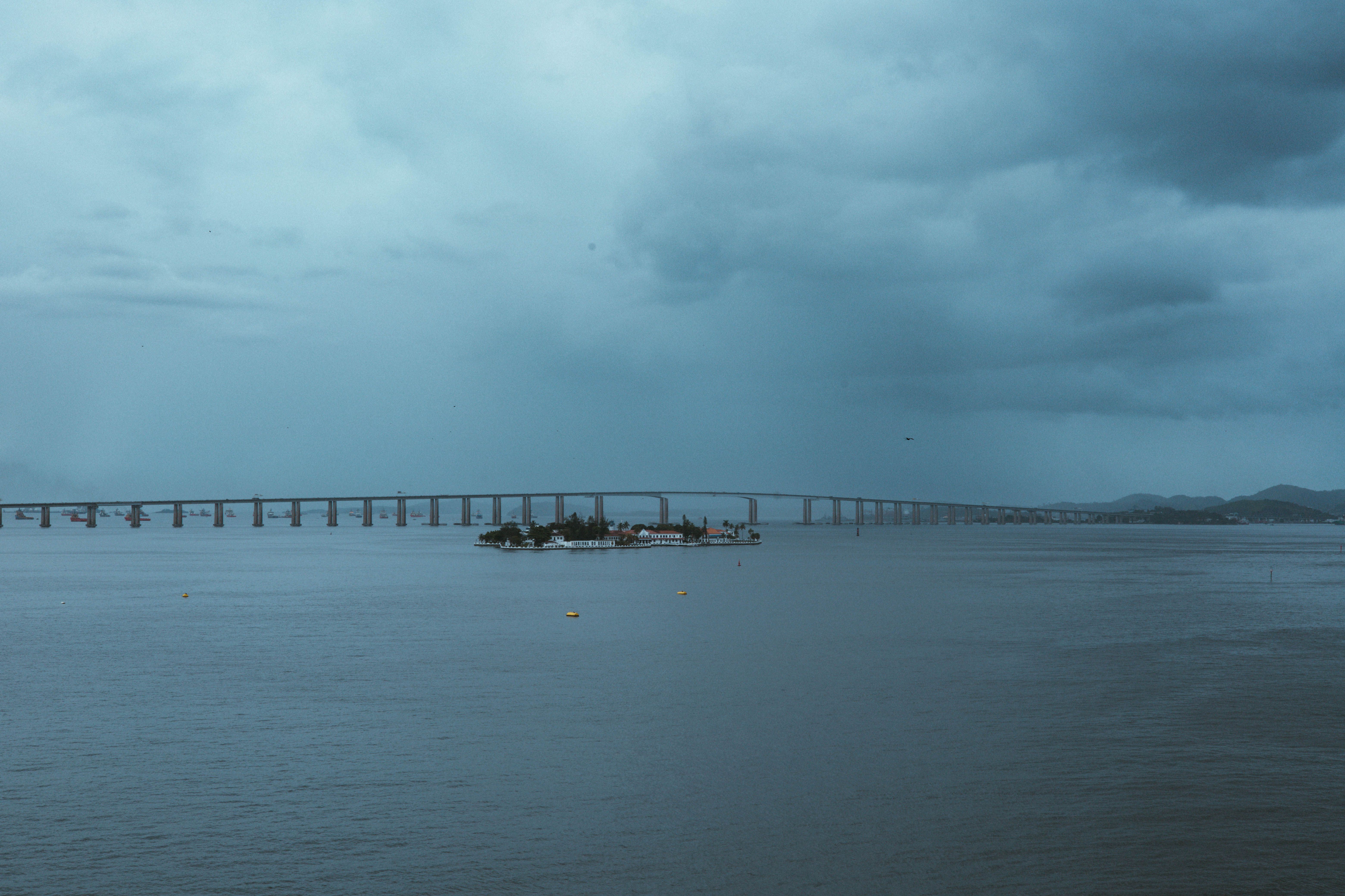 Expansive bridge extending over tranquil blue sea with a scenic backdrop of cloudy sky. — Foto: Rafael Rodrigues / Pexels